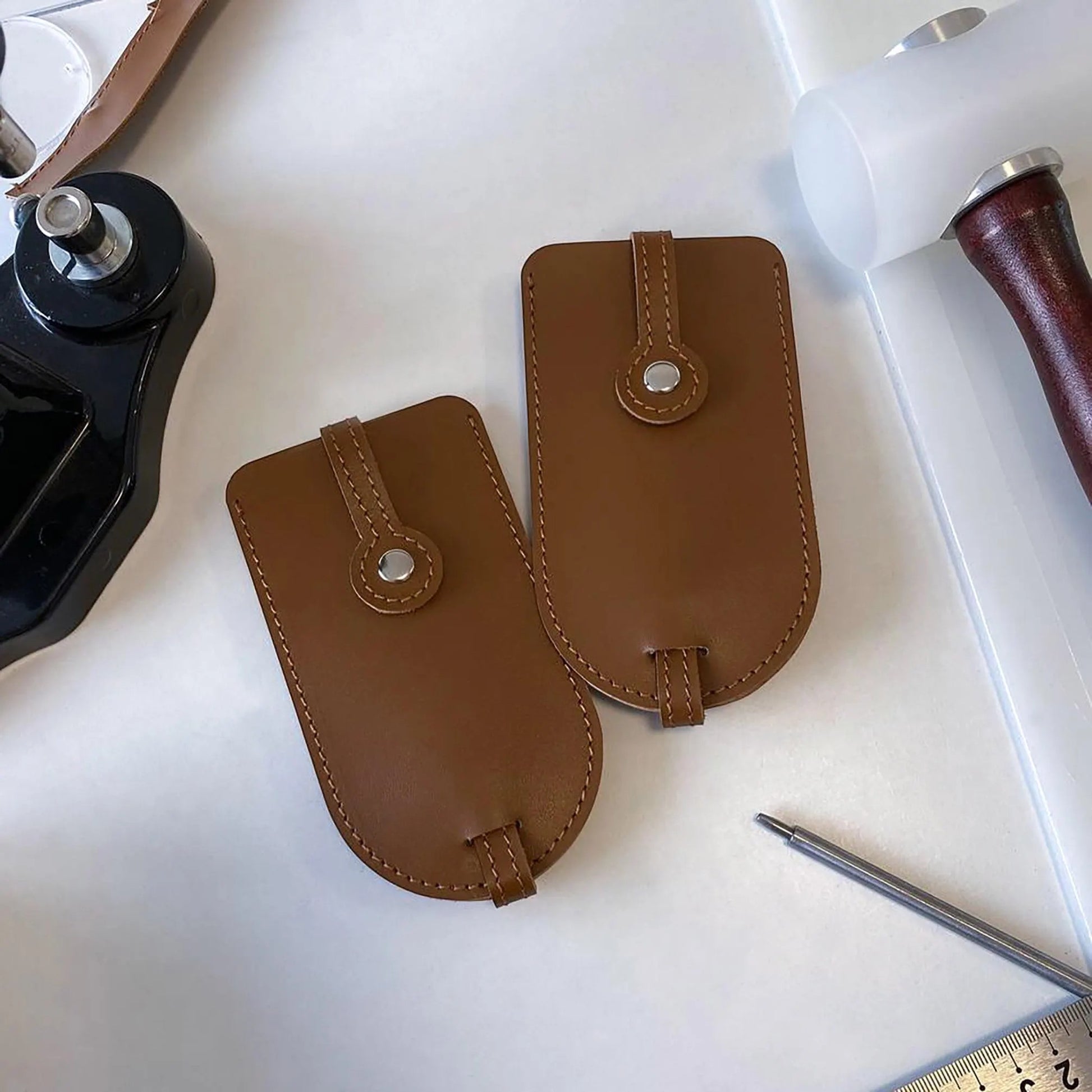 Two brown leather pouches on a white surface with a pen and ruler in the background.
